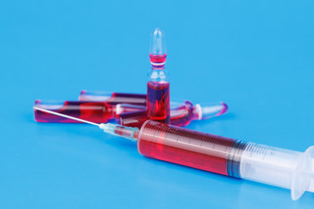 Red vitamin B12 ampoules and syringe on blue surface representing supplement and health care