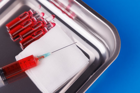 Healthcare concept with ampoules, syringe, and gauze on steel tray against blue