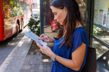 One female traveler at a bus stop examining a map to find landmarks and plan their sightseeing day in the city.の写真素材
