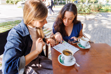 Smiling women consult a tourist map and enjoy a pleasant break under the sun.