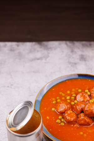 Open tin filled with meatballs and peas, rustic presentation on wooden board over cement table.の写真素材