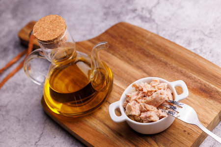 Tuna in oil in open can placed on rustic board on textured gray background.の写真素材