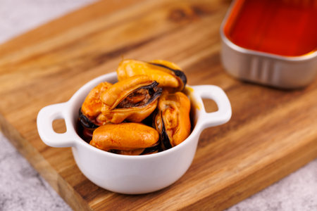 Canned seafood with vibrant orange sauce placed on rustic wood board and gray table.の写真素材