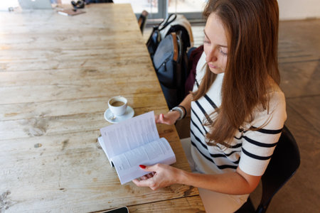 A woman enjoys her coffee while reading a book, capturing a serene moment of calm and personal timeの写真素材