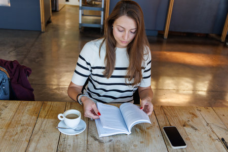 Young woman reading a book and drinking coffee in a coffee shop.の写真素材