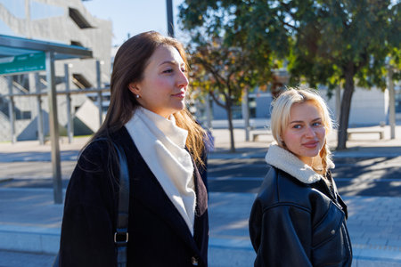 Two friends sit on the bench, enjoying a relaxed conversation while waitingの写真素材