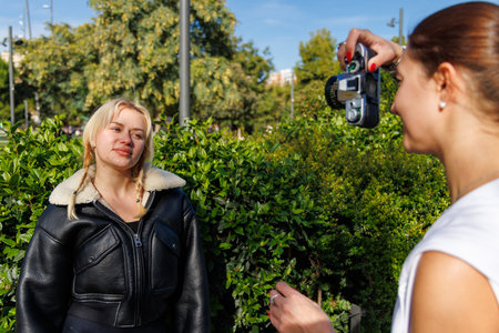 Two women walk through the park and take retro camera photos, enjoying a cheerful outdoor moment full of light.の写真素材