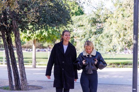 Two friends stroll through the park chatting calmly, sharing moments and enjoying a peaceful walk in a natural and open outdoor settingの写真素材