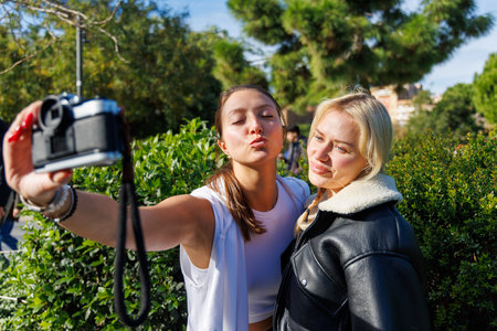 Two women take turns using a vintage camera for fun selfies as they enjoy a friendly and relaxed...