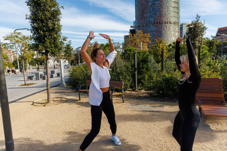 Two women in gym clothes stretch resistance bands while training outside.の写真素材