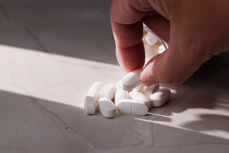 Close-up of a transparent bottle full of white pills on a white stone background.