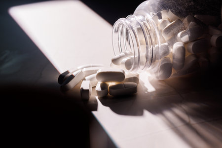 Transparent medical bottle brimming with white pills on a textured granite surface. A clean and professional image for health and wellness industry.の写真素材