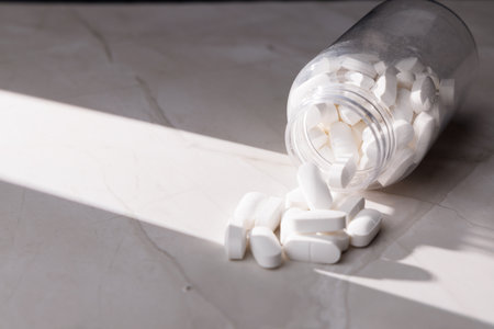 White pills inside a clear container on a luxury white granite table. High-quality imagery for...