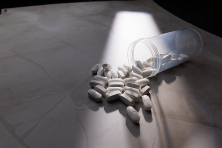 White medical capsules in a transparent container on a white granite surface illustrating healthcare...