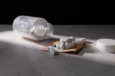 Medicine pills in a transparent bottle on euro cash notes over a white granite stone surface...