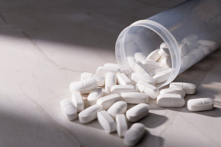 Pharmaceutical white capsules inside a transparent bottle on a white granite desk illustrating...