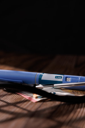 Clear shot of GLP-1 pens and a stethoscope on banknotes over dark wood showing the nature of weight loss and diabetes care servicesの写真素材