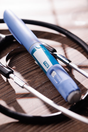 High angle view of medication pens and a stethoscope on a dark wood background representing...