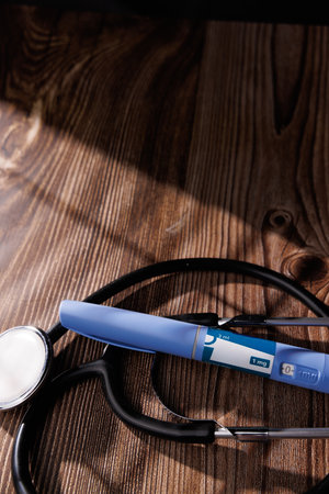 Healthcare concept featuring a pen and a stethoscope on a dark wooden tabletop representing modern pharmaceutical drugs for chronic diseasesの写真素材