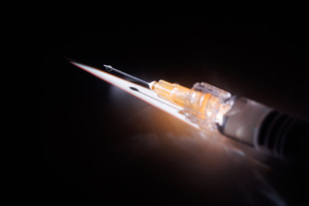 Professional shot of a glass syringe reflecting on a white marble tabletop under a light beam against a dark black background.の写真素材