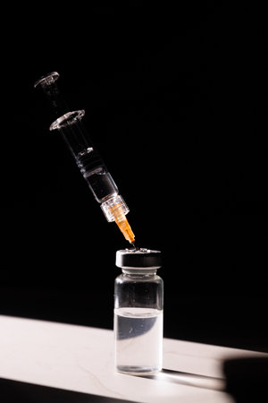 Medical glass syringe and vaccine vial on marble surface with dramatic light reflections and dark background for pharmaceutical healthcare concepts.の写真素材