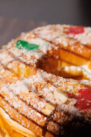 A classic Roscon de Reyes with sugar and candied fruit on a rustic wood table. The dark background highlights the texture of this Epiphany pastry!!の写真素材