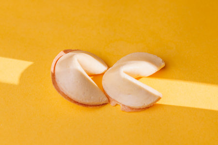 Traditional golden fortune cookies on a bright yellow surface. This iconic snack is perfect for illustrating destiny and cultural celebrations.の写真素材