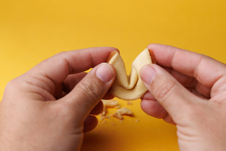 Human hands interacting with a traditional Asian fortune cookie on an intense yellow background. Symbolizing hope, destiny and future prosperity today.の写真素材