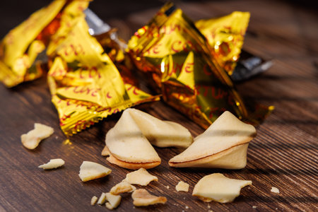 Golden fortune cookies and wrappers on a dark wooden background. The sharp light play highlights the texture of these iconic snacks for commercial.の写真素材