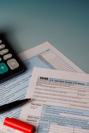 April 15 income tax filing concept with color Form 1040 and tools. Beautiful sunlight through a window on a desk with a calculator and office supplies.の写真素材