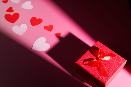 Gift box with paper hearts on pink. Perfect for illustrating tender affection, romantic dates and simple love symbols for social media photography.の写真素材
