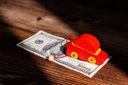 US car affordability crisis with a wooden toy car on dollar bills. Ideal for representing banking loans, auto finance and expensive rentals today.の写真素材