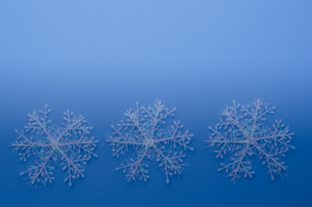 Three white snowflake ornaments in a row on lower half of page with a faded blue backgroundの写真素材