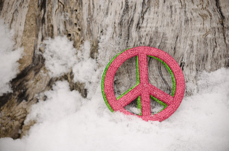 Green and red peace sign ornaments leaning against a tree in the snowの写真素材