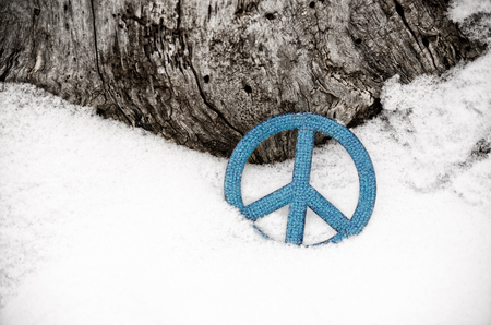 blue peace sign ornament in the snow leaning against a treeの写真素材