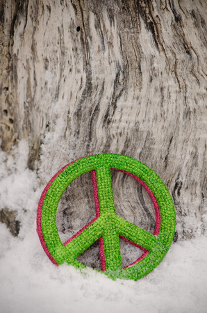 Green and red peace sign ornaments leaning against a tree in the snowの写真素材