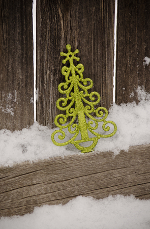 green Christmas tree ornament leaning against rustic fence in snowの写真素材