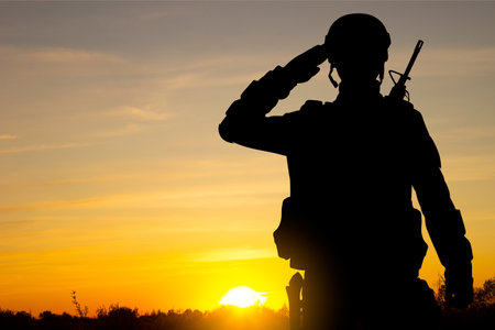 Silhouette of soldier saluting on background of sunset skyの写真素材