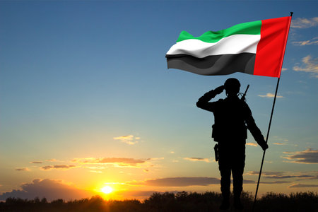 Silhouette of saluting soldier with the flag of UAE against the sunset. Armed forces of United Arab...