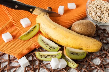 Cutting kiwi and banana on orange napkin with flakes in bowlの写真素材