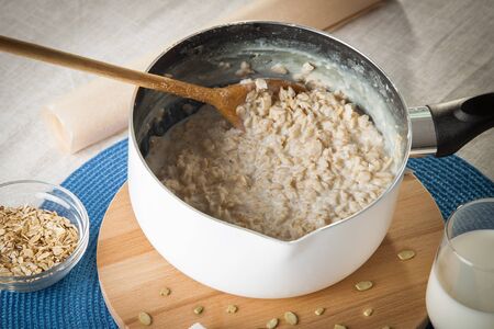 Cooking porridge in a bowl with wooden spoon on the tableの写真素材