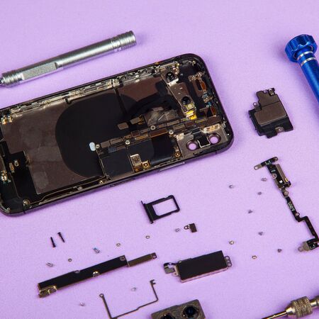 Moblile phone disassembled for battery replacement with screwdrivers on purple bachground.の写真素材