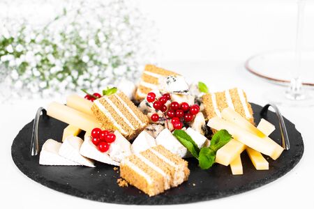 Black cheese plate with red berries and cake isolated on white tableの写真素材