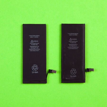 Two batteries for cell phones new and old comparison repair on a green background top view.