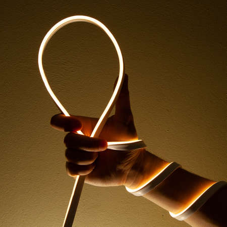Flexible white led tape neon in hand on black background.の写真素材