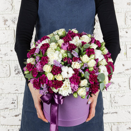 Florist woman in blue denim apron holding fresh blossoming flower bouquet in paper round box over brick wall.の写真素材
