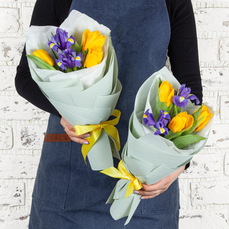 Florist woman in blue denim apron holding fresh blossoming flower bouquet wrapperd in paper over brick wall.の写真素材