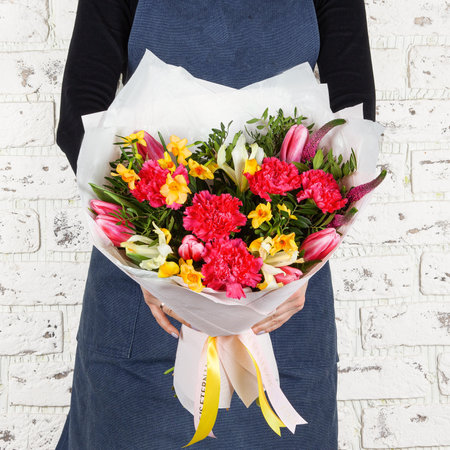 Florist woman in blue denim apron holding fresh blossoming flower bouquet wrapperd in paper over brick wall.の写真素材