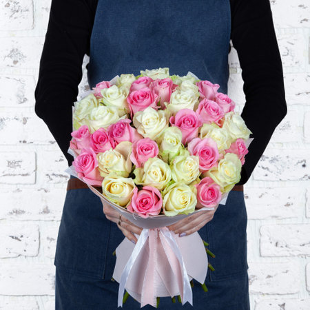 Woman florist holding freshly made white and pink roses blossoming flower bouquet on brick wall background.の写真素材