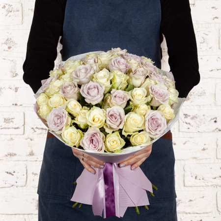Woman florist holding freshly made blossoming flower bouquet on brick wall background.の写真素材